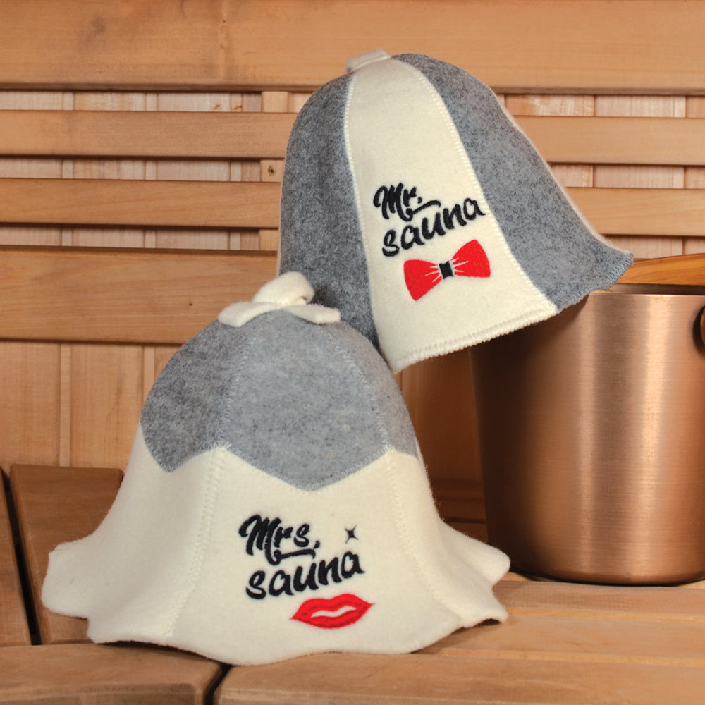 Pair of light grey and white wool sauna hats. One hat features the text 'Mrs. Sauna' and a red lips graphic. The other hat features the text 'Mr. Sauna' and a red bow tie graphic. Both hats have a loop at the top.