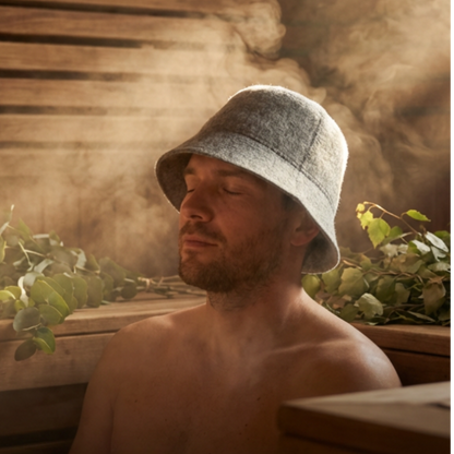 Man sitting in a steam room with bucket hat and plants around
